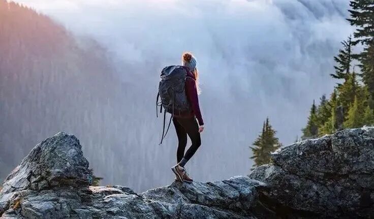 This may contain: a person with a backpack standing on top of a mountain looking at the clouds below
